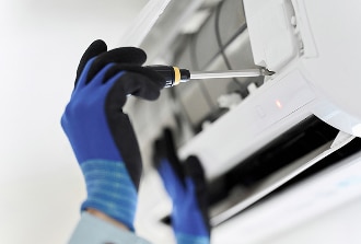 Réparation climatisation : service d'entretien par un technicien. Un technicien en gants bleus répare une unité de climatisation murale à l'aide d'un tournevis pour l'entretien.